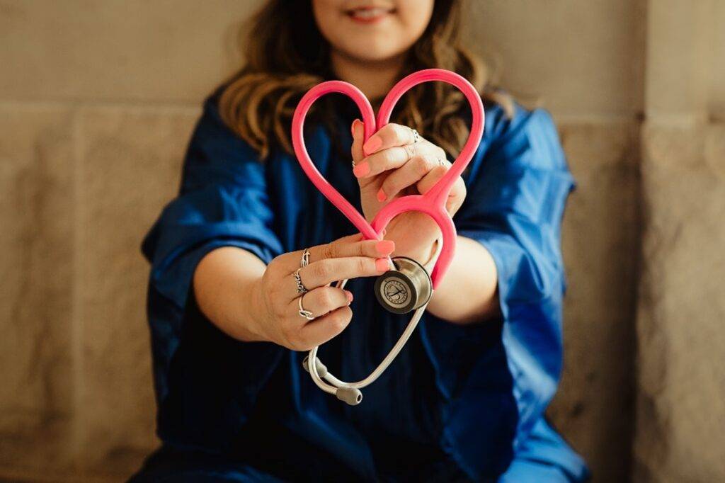 The Path to Diagnosis 2 a woman in dark blue scrubs holding a red stethoscope towards the camera and forming a heart shape with the lines of the scope